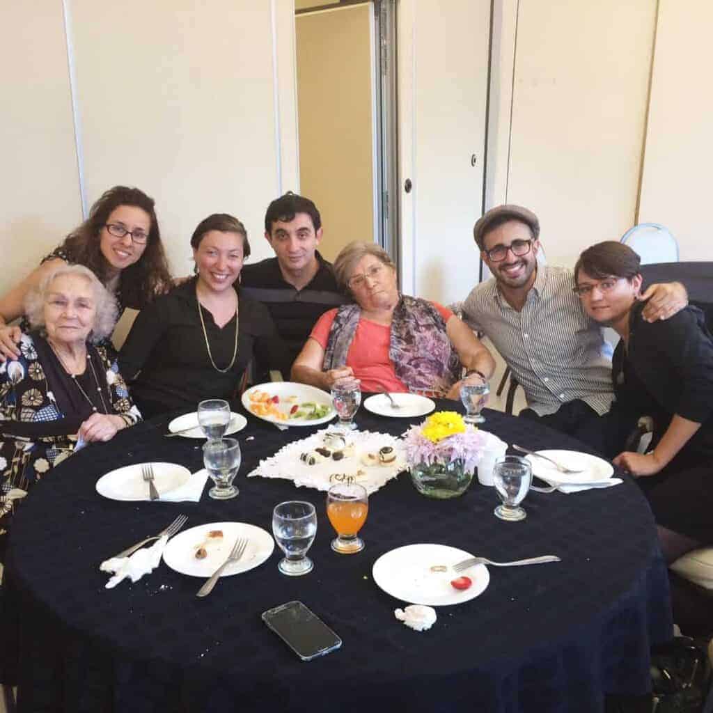 Seven people smiling and posing around a dining table with empty plates and glasses, capturing the joy of shared moments often highlighted in any Argentina travel guide.