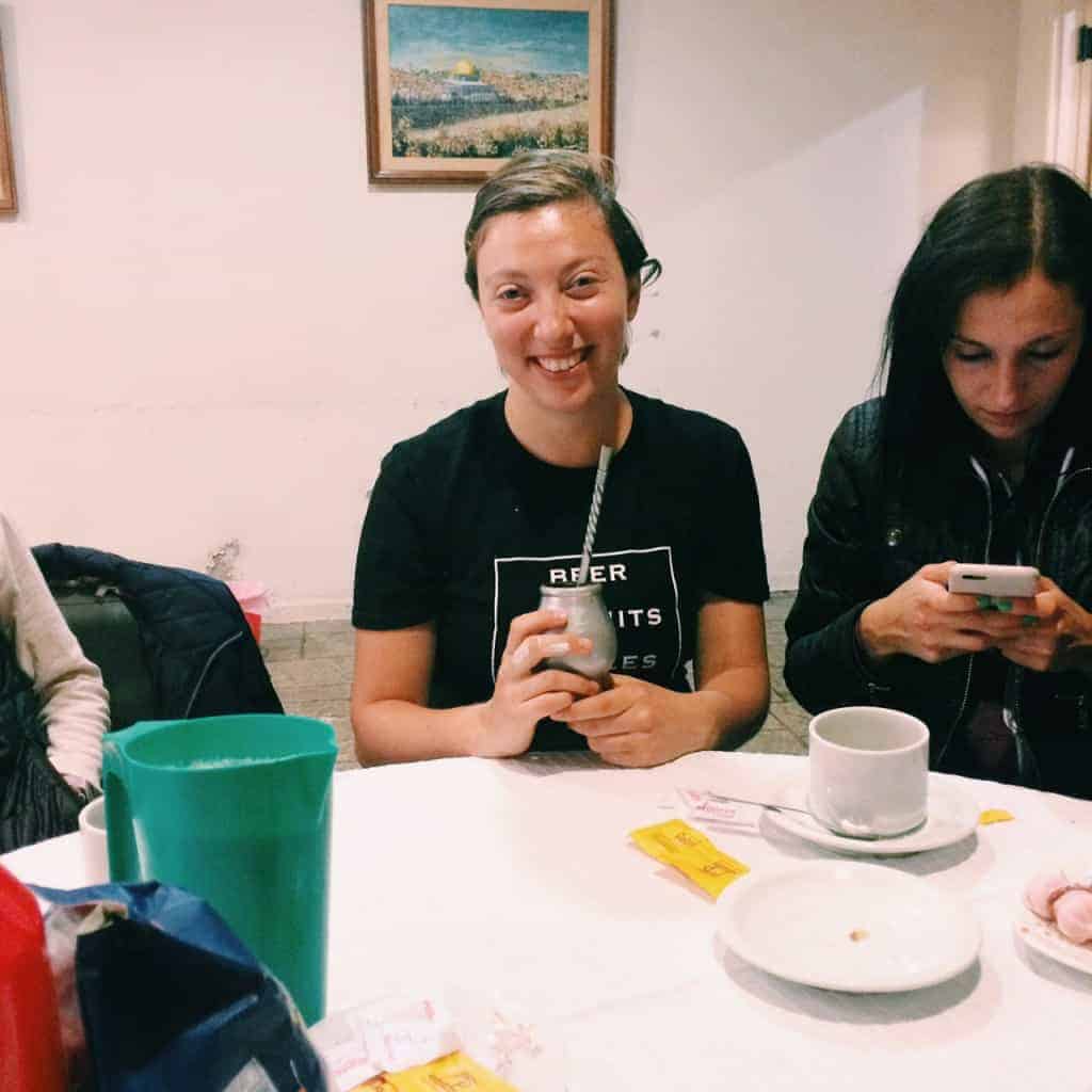 Woman smiling at a table while holding a drink, another woman next to her looks at her phone, perhaps checking the latest tips from an Argentina travel guide.