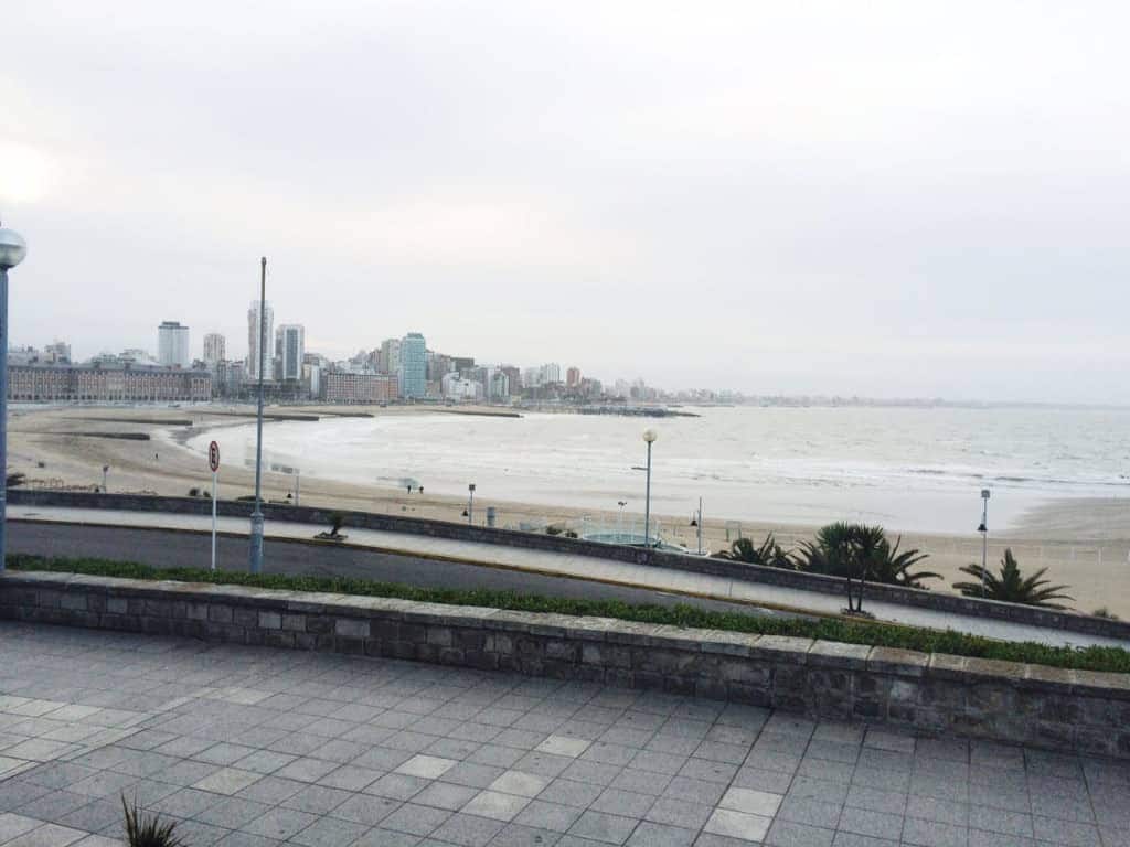 Overcast beach scene with city buildings in the background and waves along a mostly empty shore, reminiscent of coastal destinations featured in an Argentina travel guide.