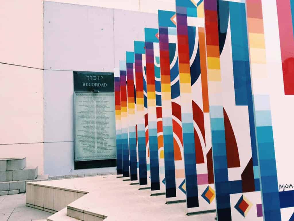 Colorful geometric panels stand in front of a memorial wall with text and names engraved on it, a striking scene often highlighted in an Argentina travel guide.