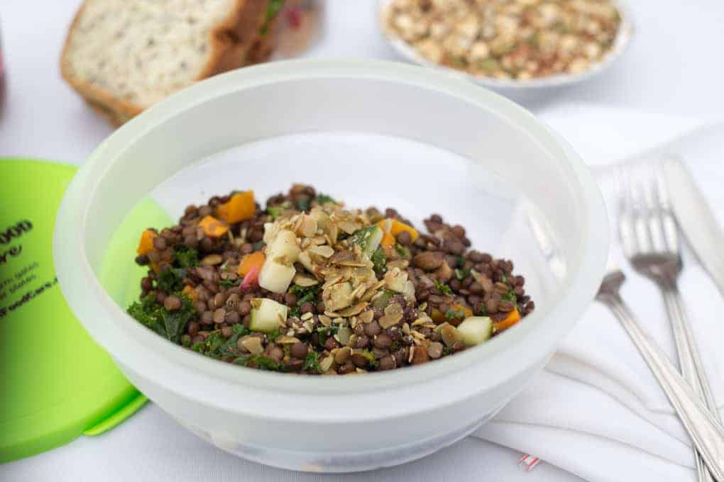 A plastic bowl of lentil salad with chopped vegetables and seeds sits on a picnic table with bread and cutlery nearby, reflecting the fresh, local focus championed by Farm and Food Care Ontario.