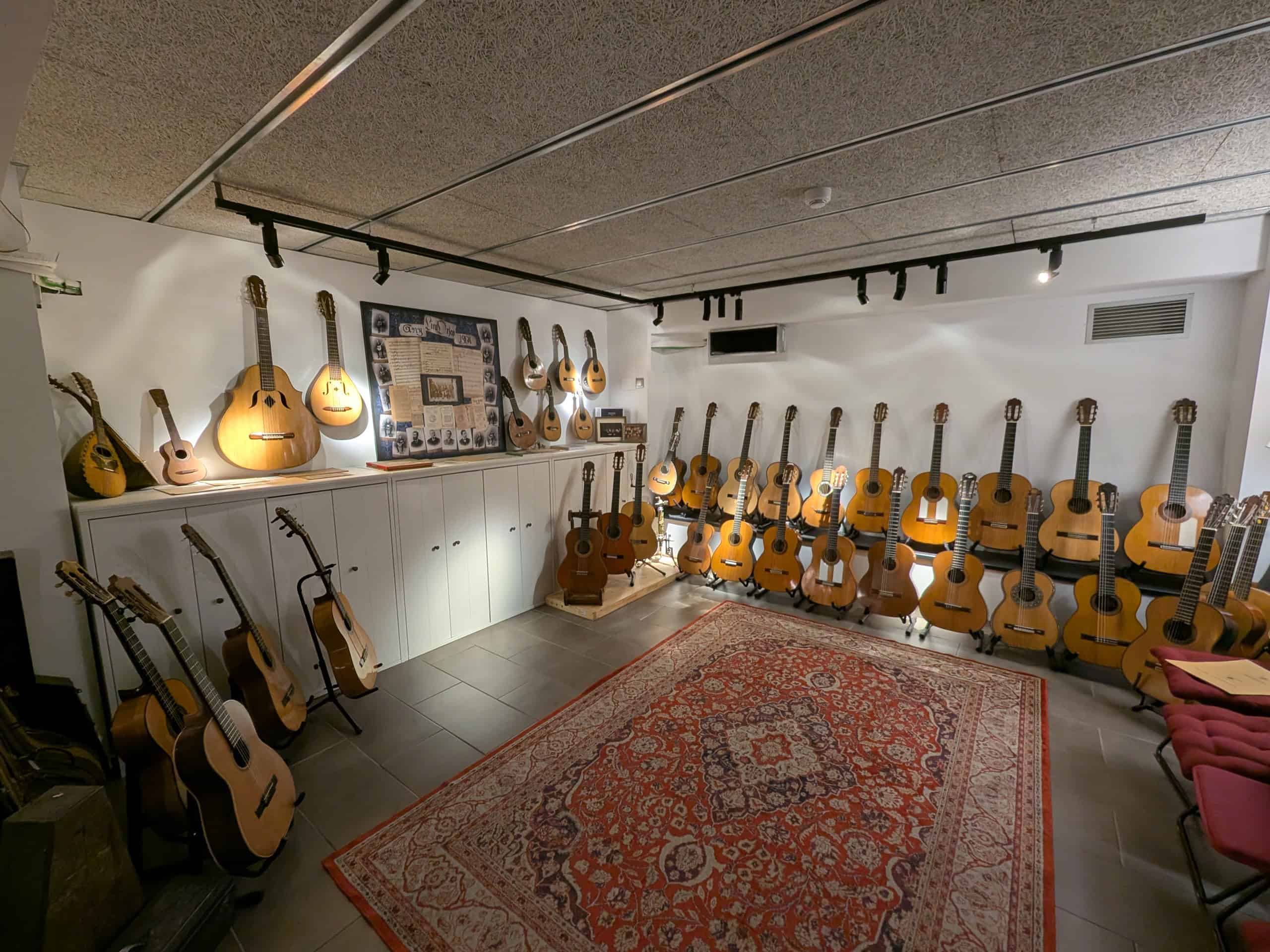 A well-lit room with guitars and stringed instruments displayed on walls and stands, a patterned rug on the floor, and framed memorabilia above white cabinets—perfect inspiration for planning your Barcelona family vacation.