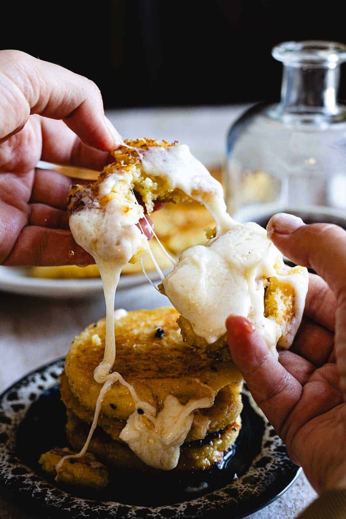 Hands pulling apart a gooey, cheesy fried cornbread cake—a delicious example of traditional vegetarian Colombian dishes—with melted cheese stretching between pieces.