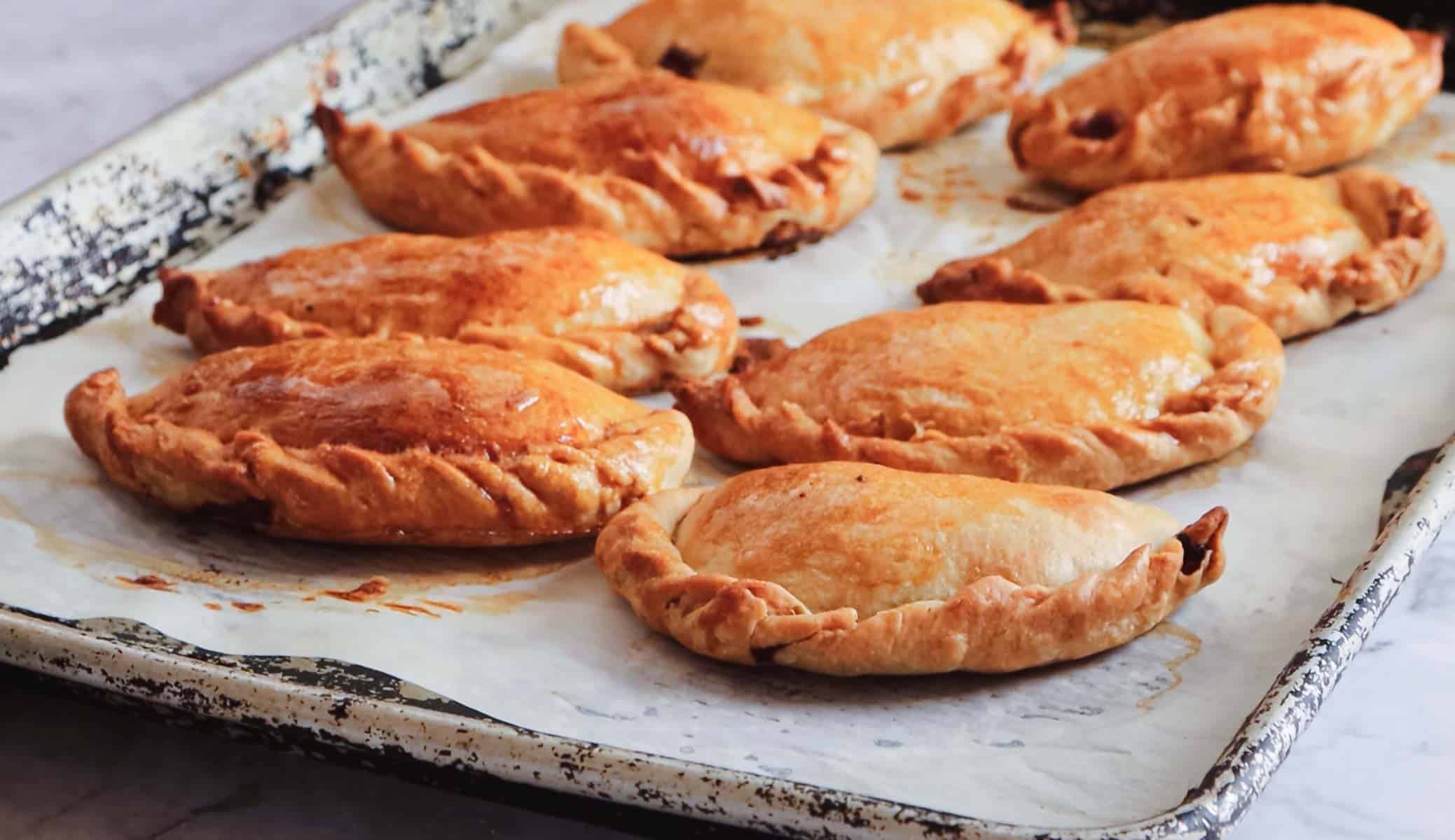 Golden brown pasties with crimped edges on a parchment-lined baking tray, inspired by traditional vegetarian Colombian dishes.