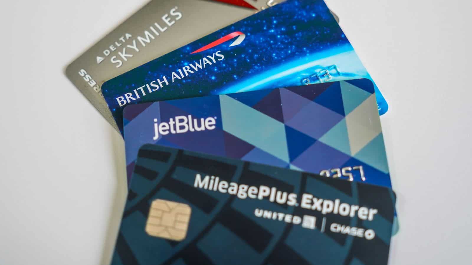 A close-up of four overlapping airline credit cards, including Delta SkyMiles, British Airways, JetBlue, and United MileagePlus Explorer, displayed on a white surface.
