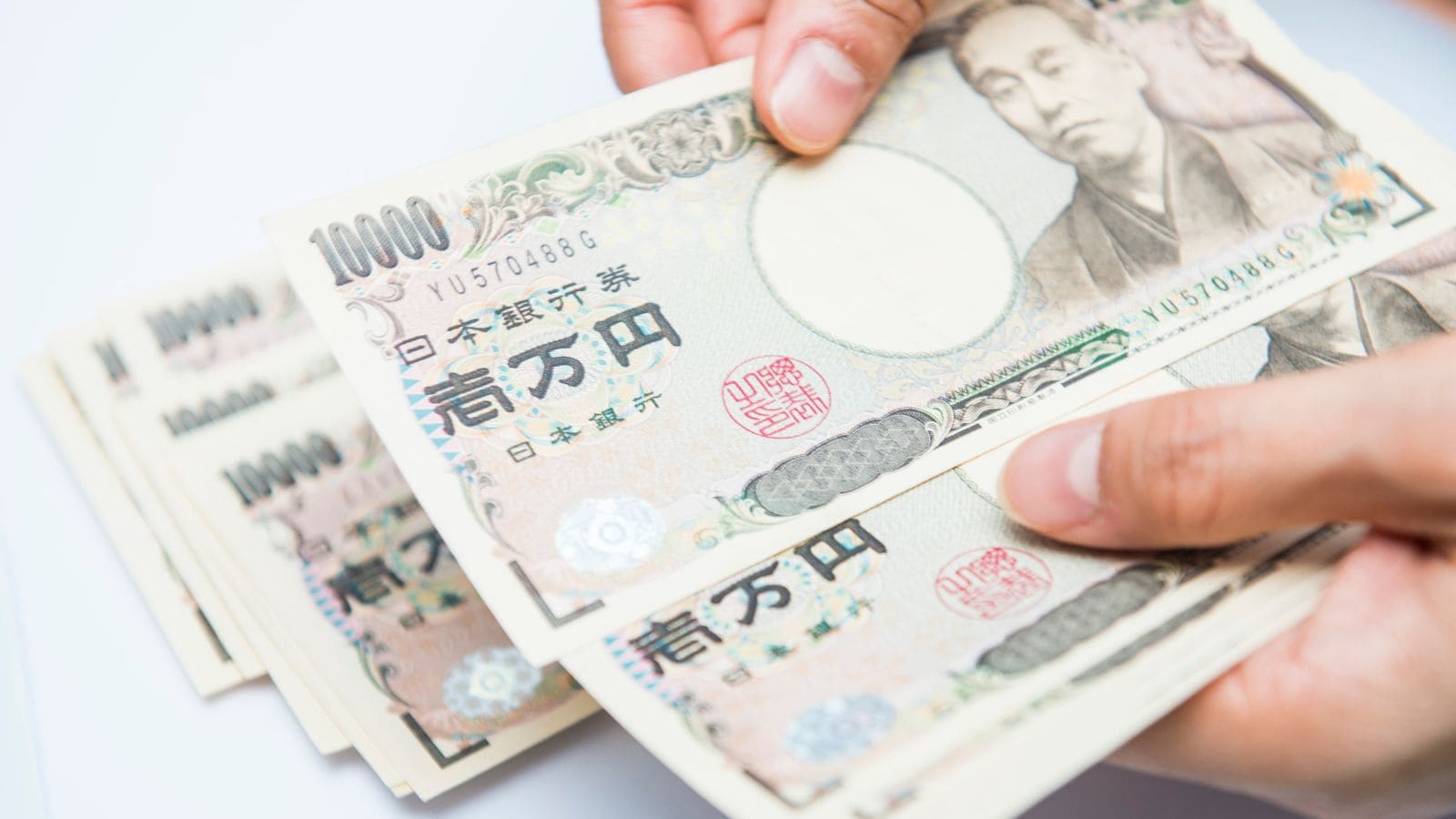 A person holding and counting several Japanese 10,000 yen banknotes, with the bills fanned out and the portrait of Yukichi Fukuzawa visible on the notes.