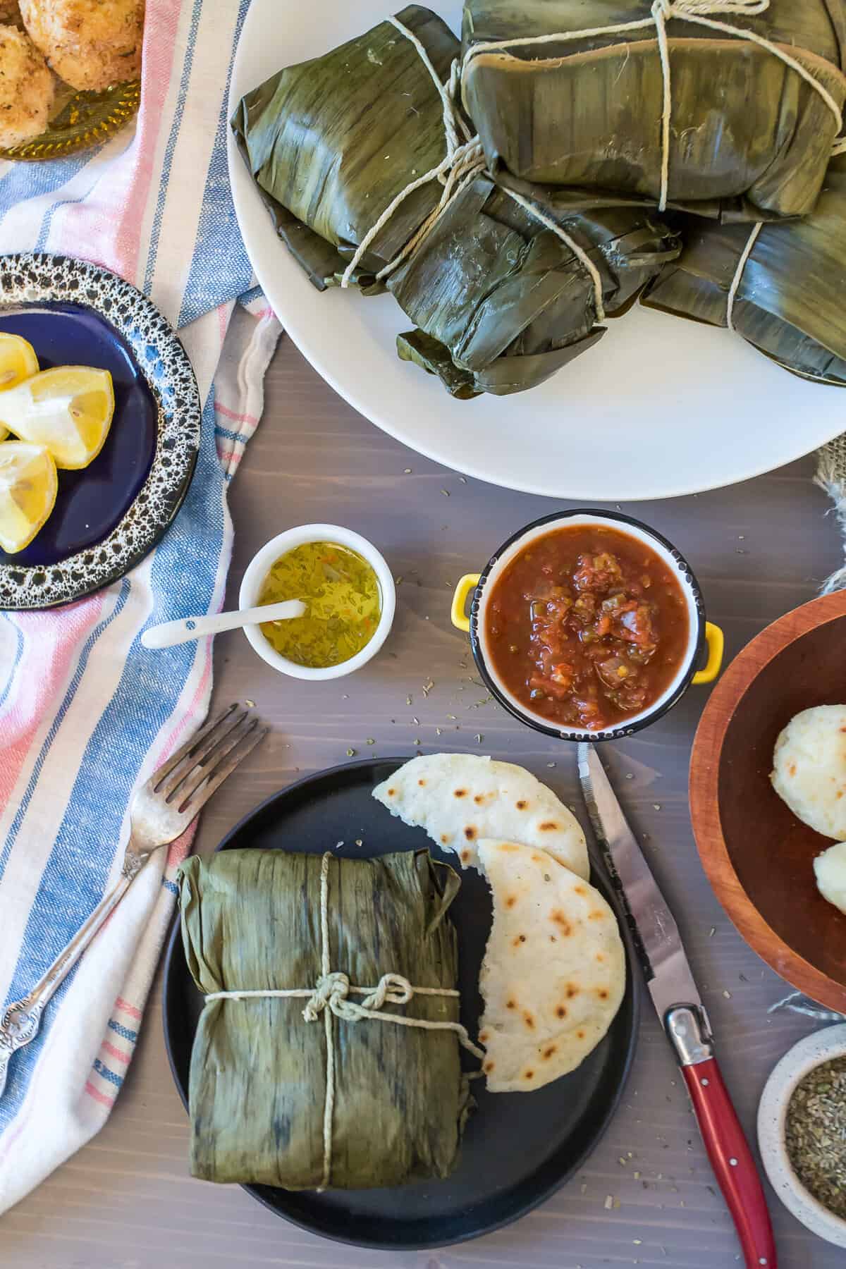 A plate with tamales wrapped in banana leaves, tortillas, salsa, and lemon slices on a table—perfect examples of traditional vegetarian Colombian dishes.