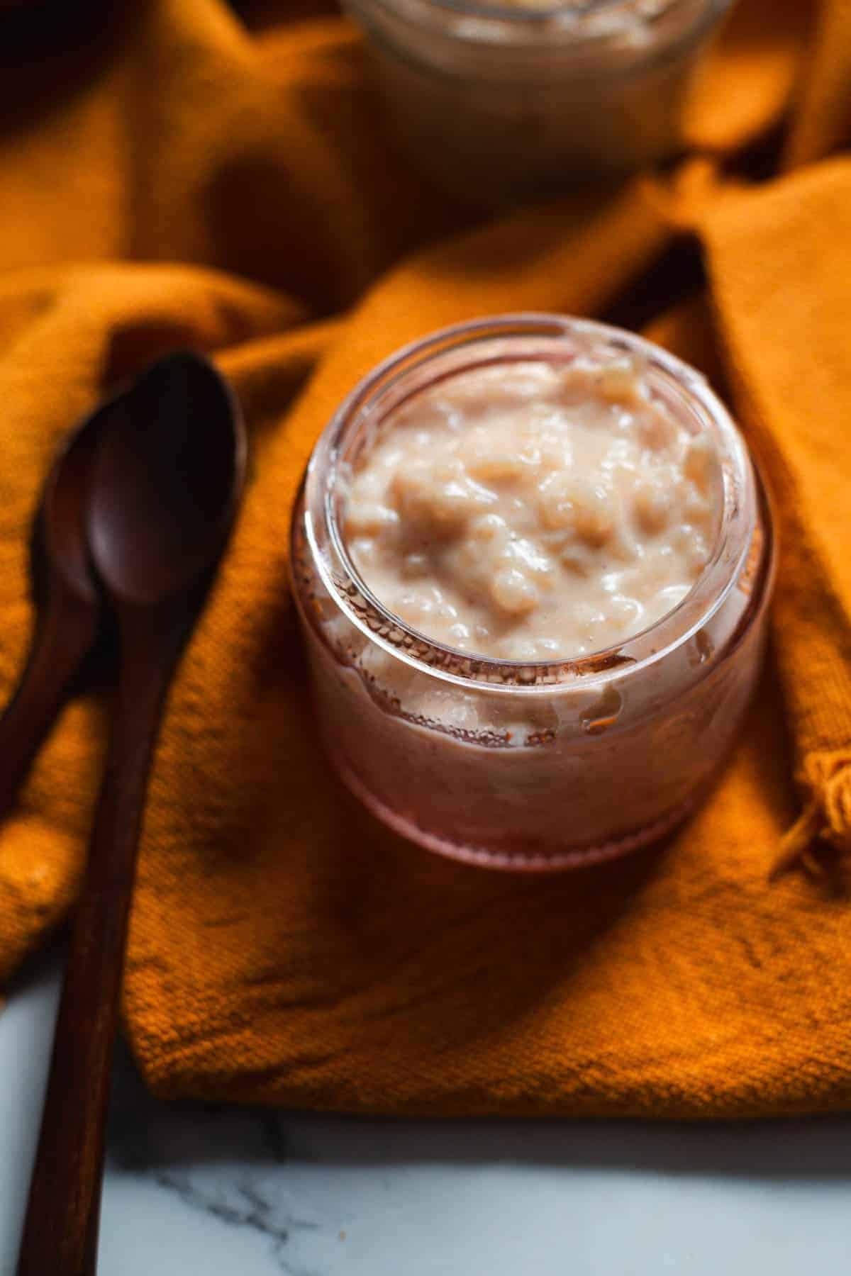 A glass bowl of rice pudding, a classic among traditional vegetarian Colombian dishes, sits on an orange cloth with two wooden spoons beside it.