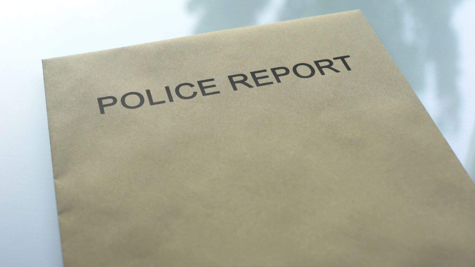 A brown folder labeled "Police Report" in black text is placed on a light-colored surface. The folder appears closed and is the main focus of the image.