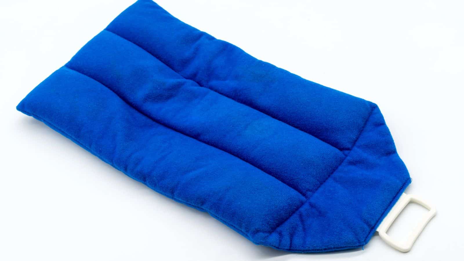 A rectangular blue microwavable heating pad with stitched channels and a white plastic handle on one end, lying on a white surface.