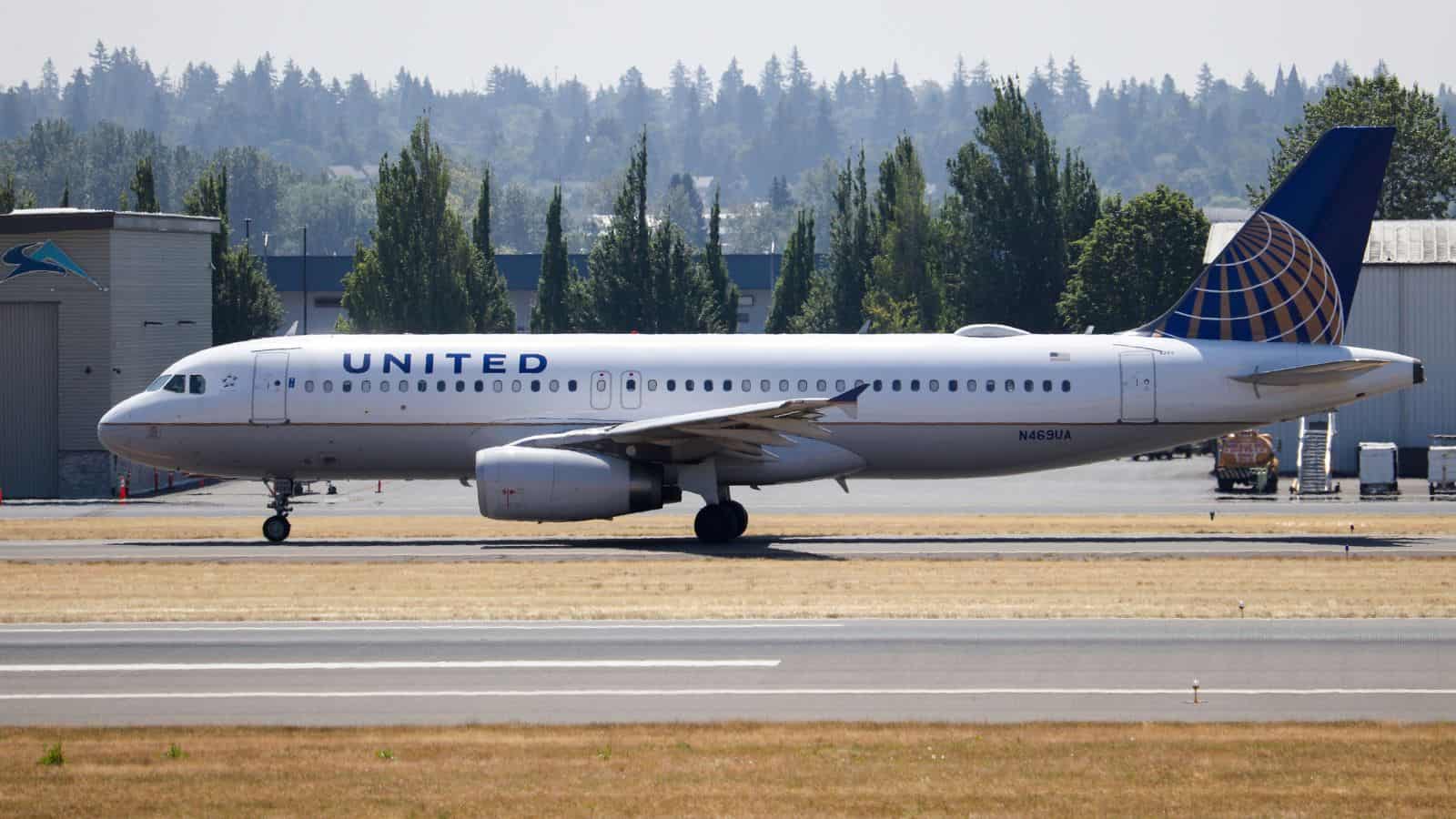 A United Airlines Airbus A320 with registration number N459UA is taxiing on a runway, with trees and buildings visible in the background.