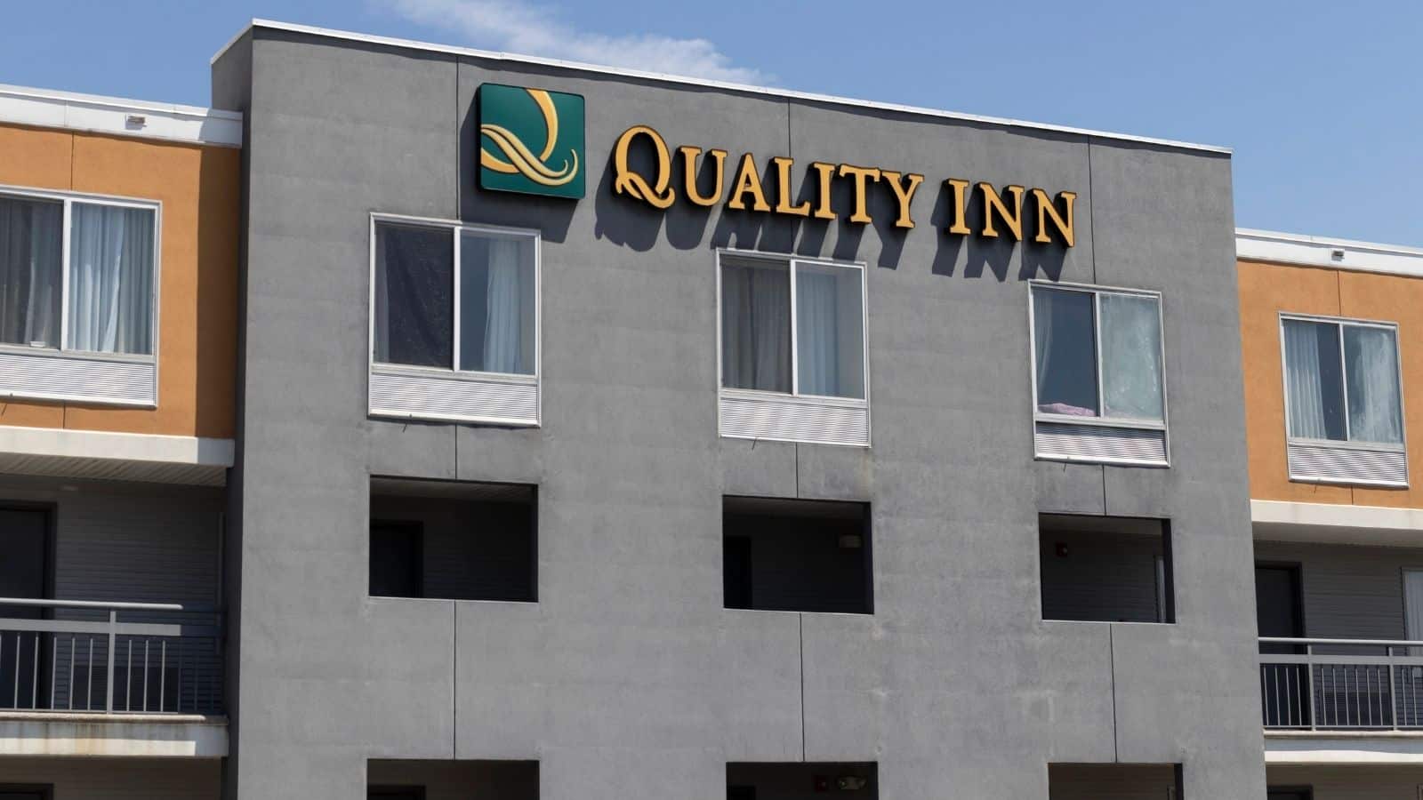 The exterior of a Quality Inn hotel building, part of the US hotel chains disappointing guests, features yellow and green signage, several windows, and balcony railings, photographed during the day.