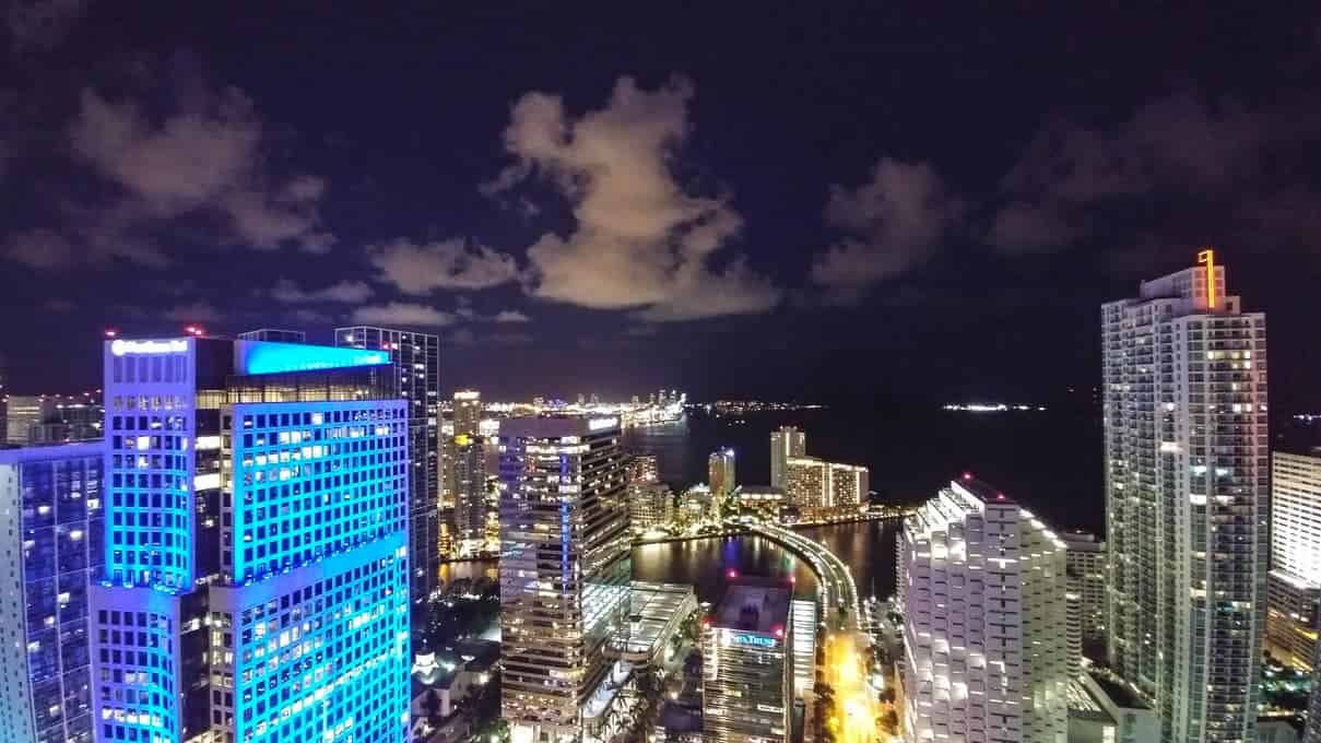 Aerial view of a city skyline at night with illuminated buildings and a dark sky with clouds.