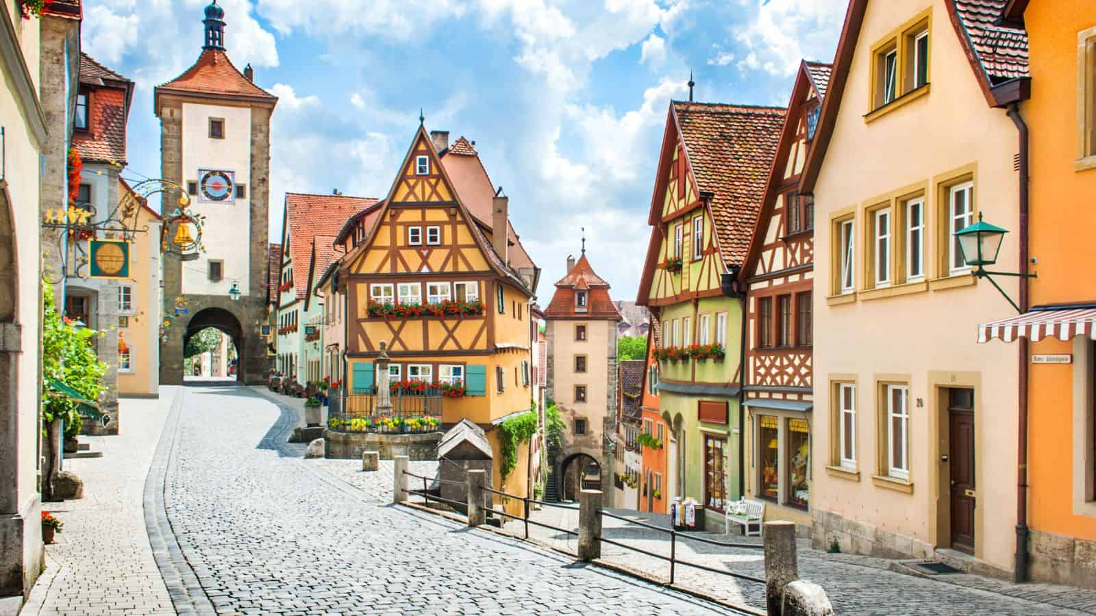 Colorful, half-timbered houses and a cobblestone street in a quaint European town with a medieval gate tower.