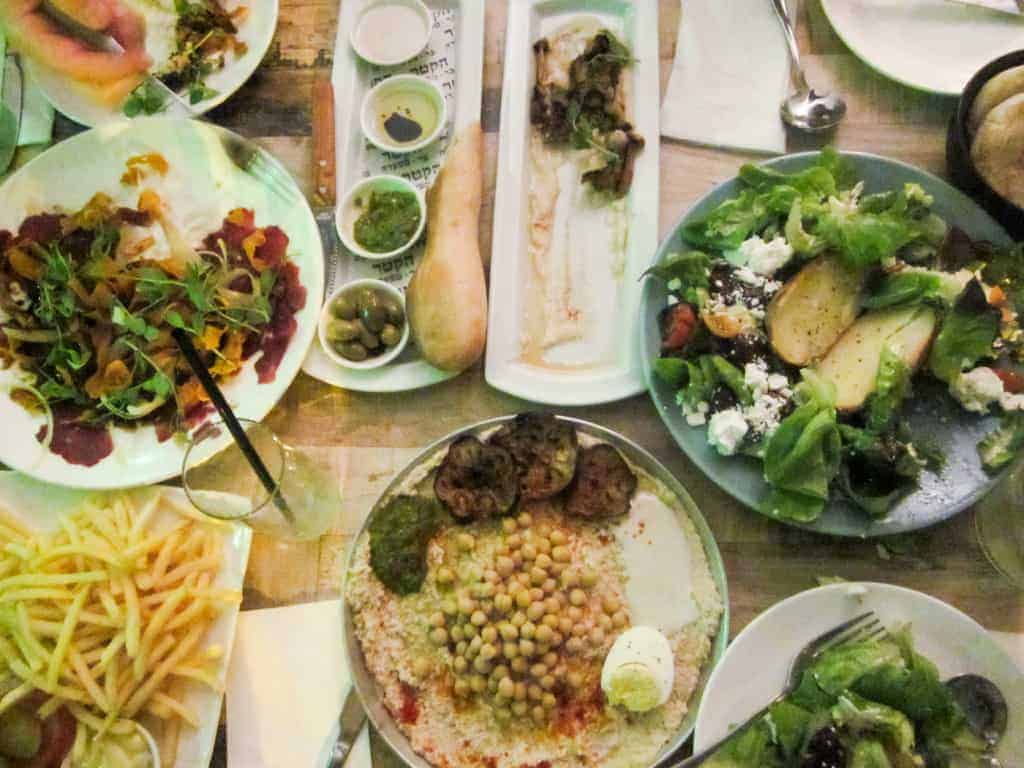 Various Mediterranean dishes on a table, including hummus, salad, fries, bread, and small bowls of dips.
