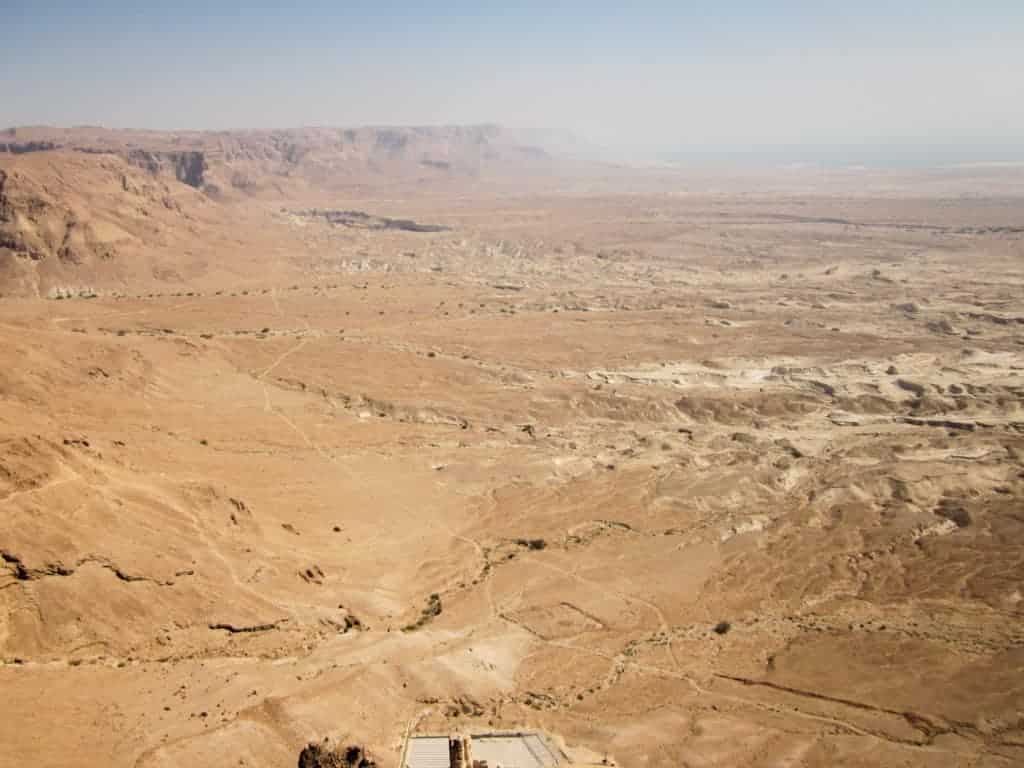 Expansive desert landscape with rocky hills and mountains under a hazy sky.