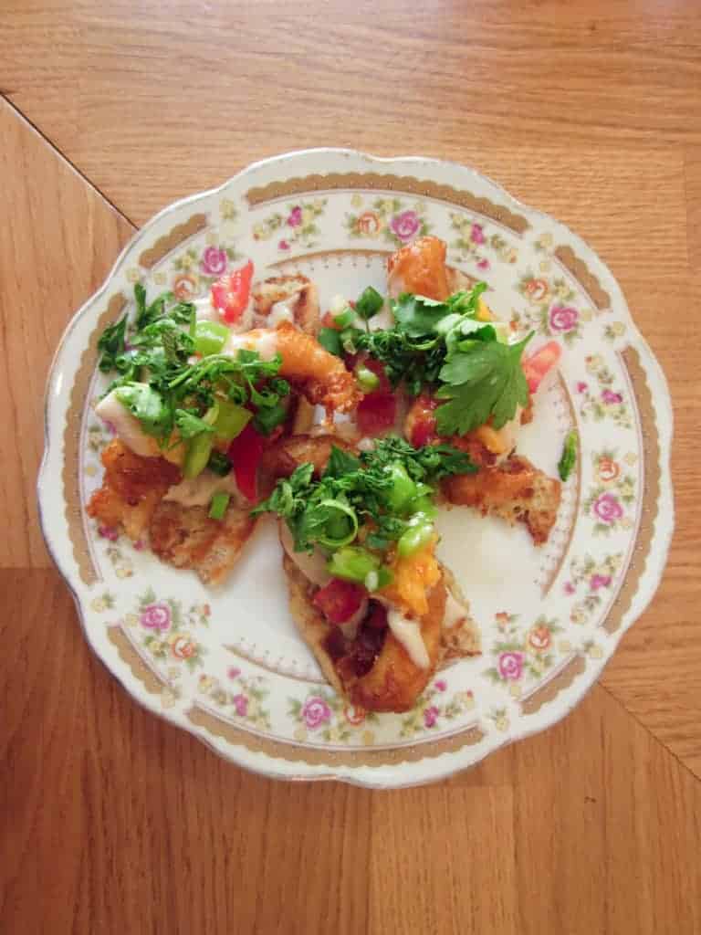 Three pieces of toast topped with veggies, herbs, and fried fish on a floral-patterned plate.