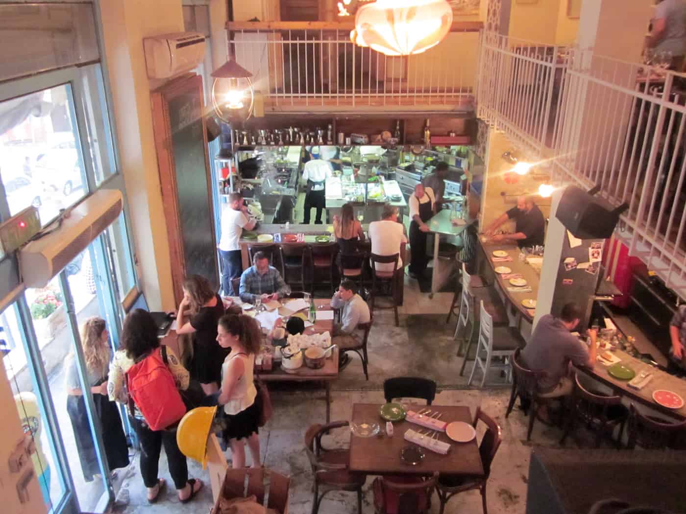 Busy café with people dining, chatting, and staff working behind the counter in a cozy, rustic interior.
