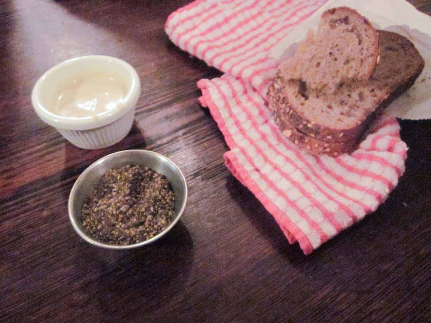 Slices of multigrain bread on a red striped towel with dishes of butter and ground black pepper.