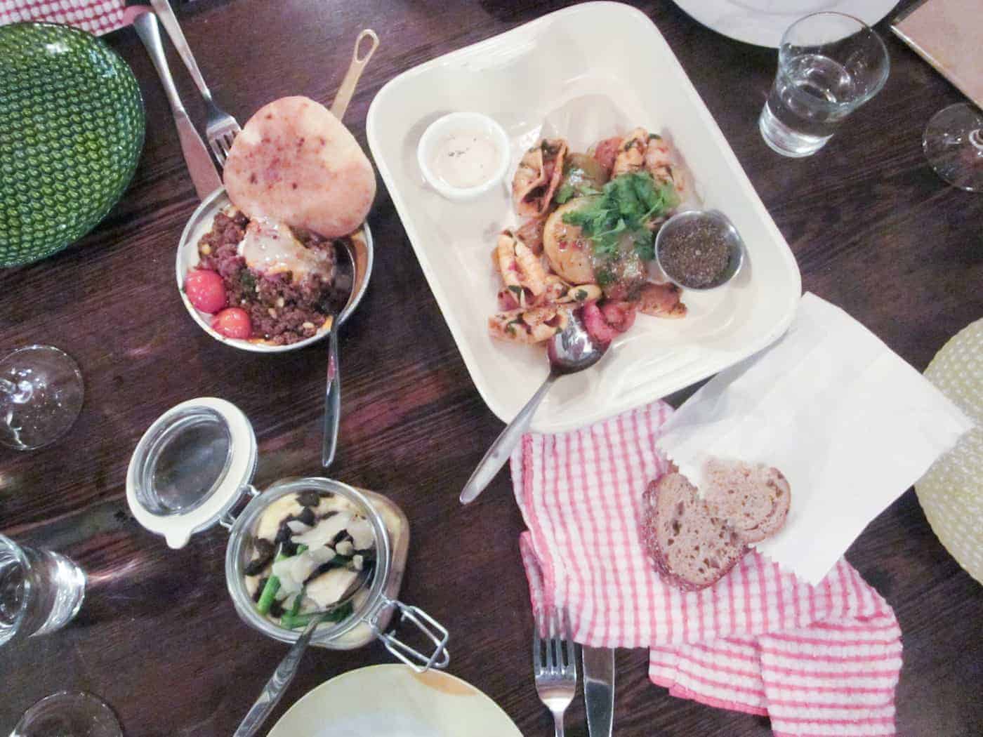 Overhead view of a table set with pasta, bread, a burger, salad, and glasses of water.