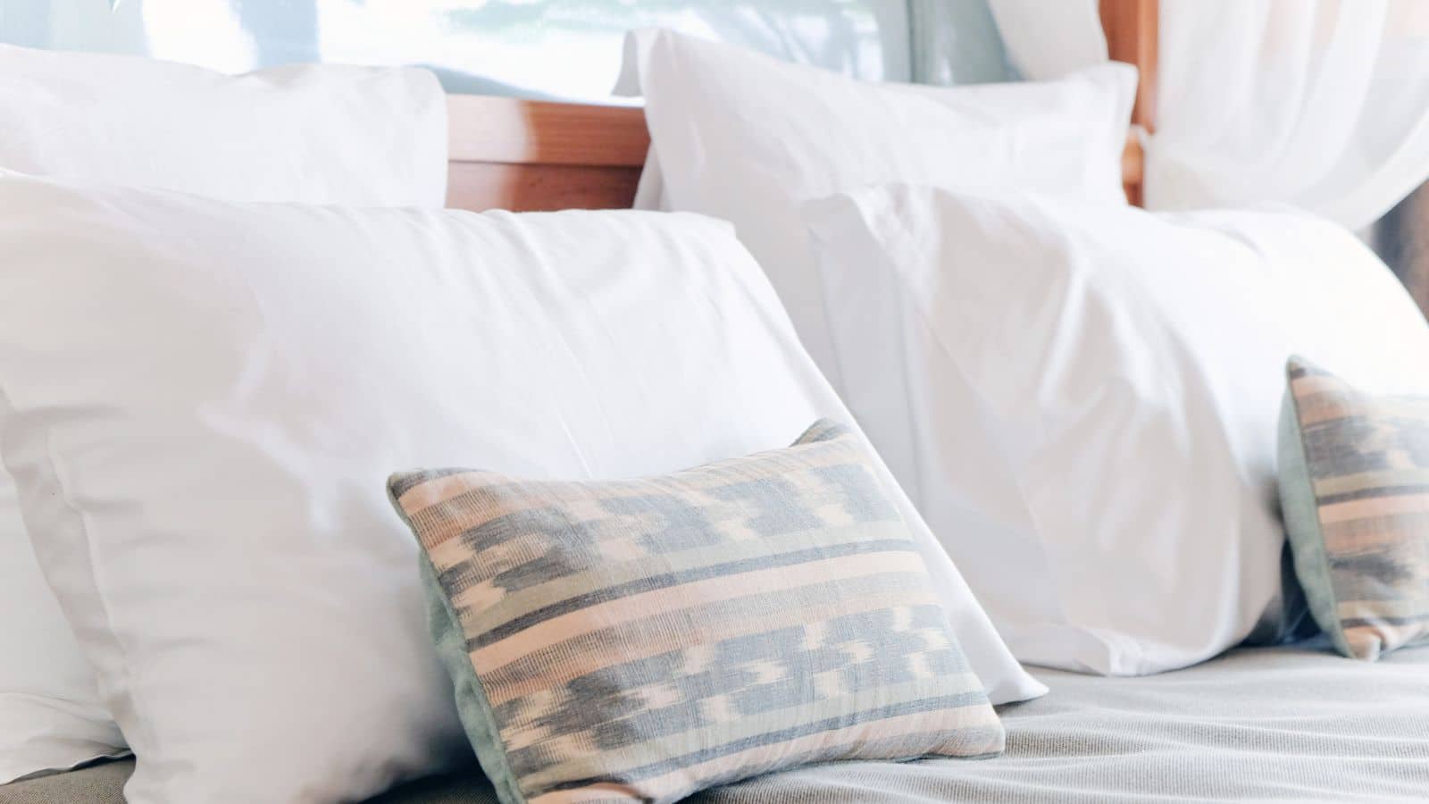 Several white pillows and two patterned cushions arranged neatly on a neatly made bed.