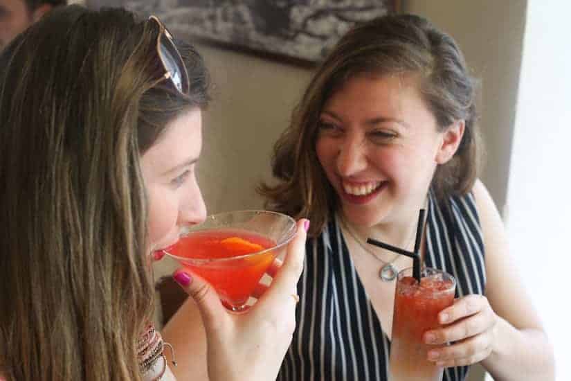 Two women smiling and enjoying red cocktails together in a bright, casual setting.