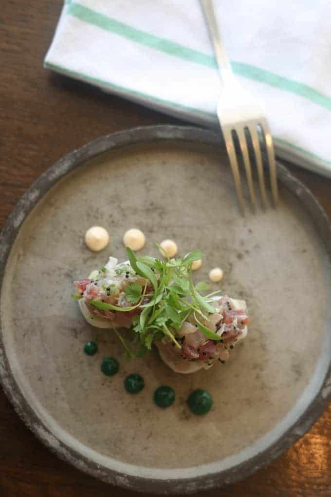 A plated gourmet dish with microgreens, sauces, and a fork on a napkin in the background.