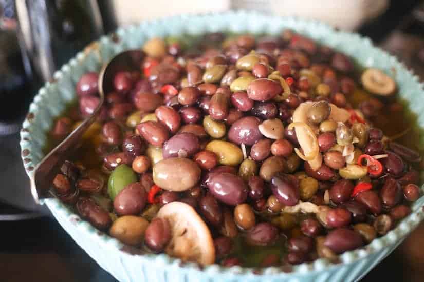 A bowl of assorted marinated olives with lemon slices and a serving spoon.