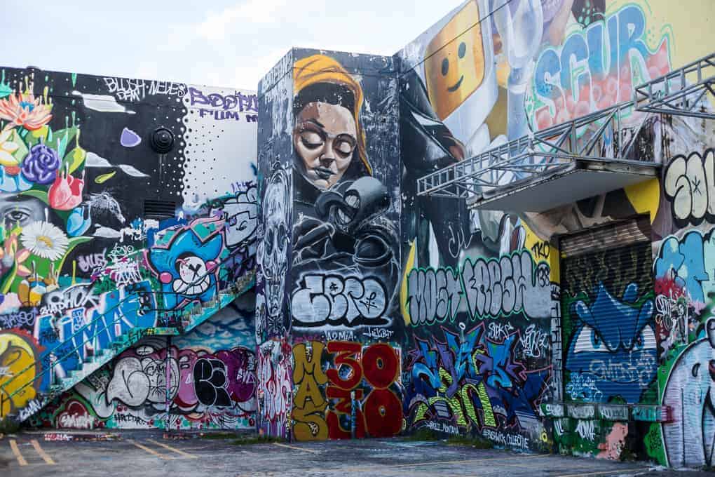 Vibrant graffiti and murals cover the walls of an urban building, including a large face in the center.