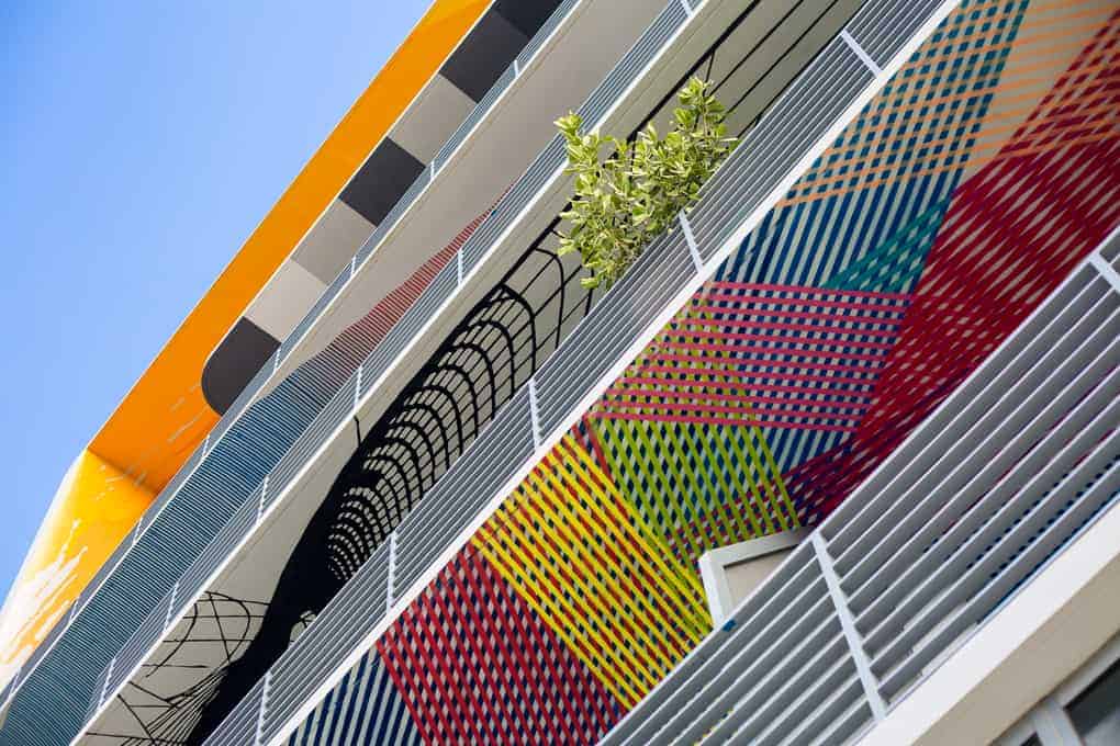Colorful geometric murals decorate the exterior of a modern building with railings and a small tree.
