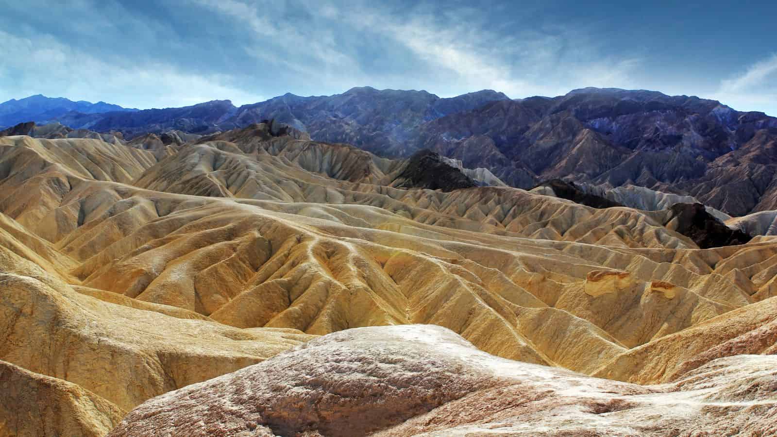 Eroded, golden-brown hills and ridges under a blue sky with mountains in the distance.