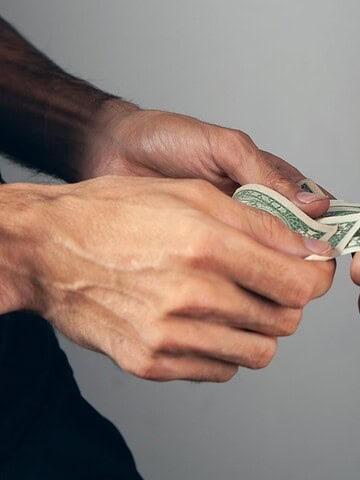 Two people exchanging a U.S. dollar bill, each holding one end of the money with their hands.