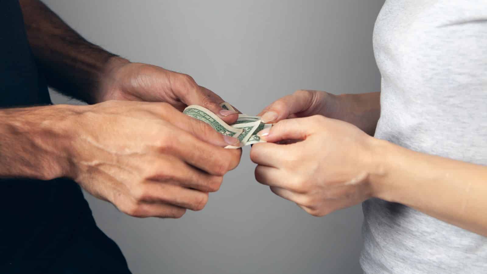 Two people exchanging a U.S. dollar bill, each holding one end of the money with their hands.