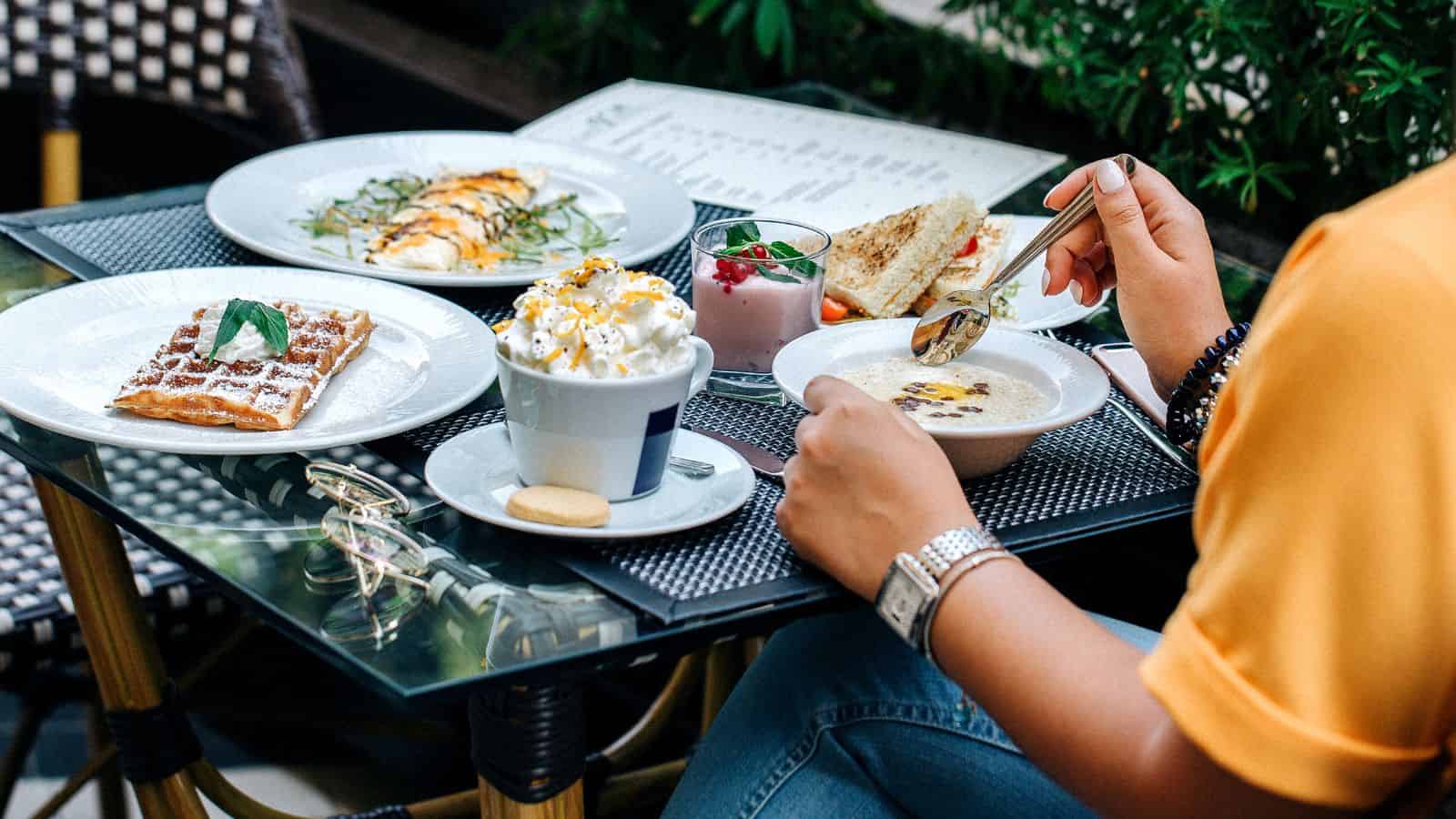 A person enjoys breakfast with waffle, omelette, oatmeal, yogurt parfait, and coffee at an outdoor café table in Paris—just like the locals do, avoiding common tourist mistakes.