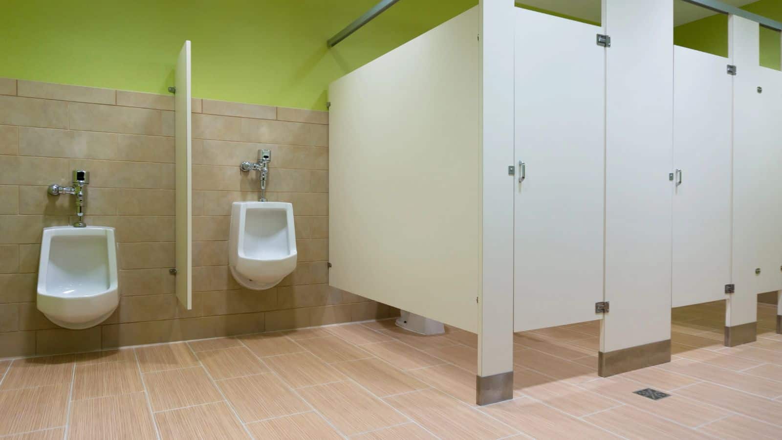 A public restroom with two white urinals mounted on a tiled wall to the left and three closed white stall doors to the right—a classic example of U.S. things that might make visitors from other countries jealous of its clean, organized design.