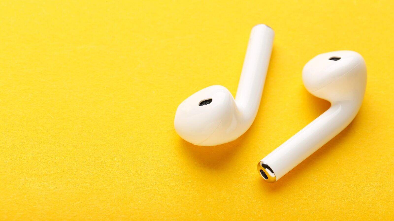 Two white wireless earbuds, commonly lost at U.S. airports, are placed on a bright yellow surface, positioned diagonally with one earbud slightly overlapping the other.
