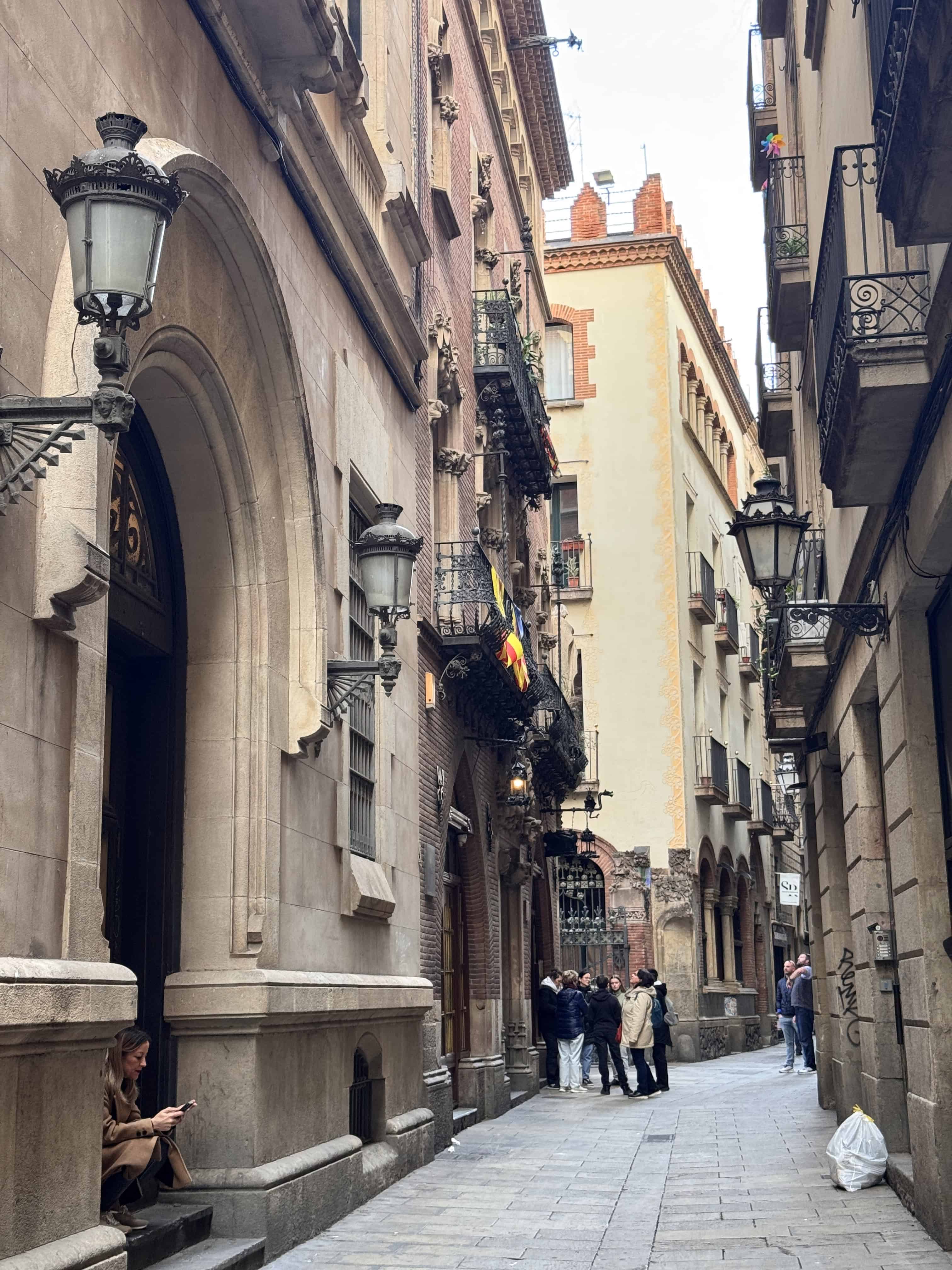 Narrow European street with old buildings, balconies, and street lamps—families gather or sit along the sidewalk, savoring moments that echo the charm of a 7-Day Itinerary on an MSC Fantasia Cruise.