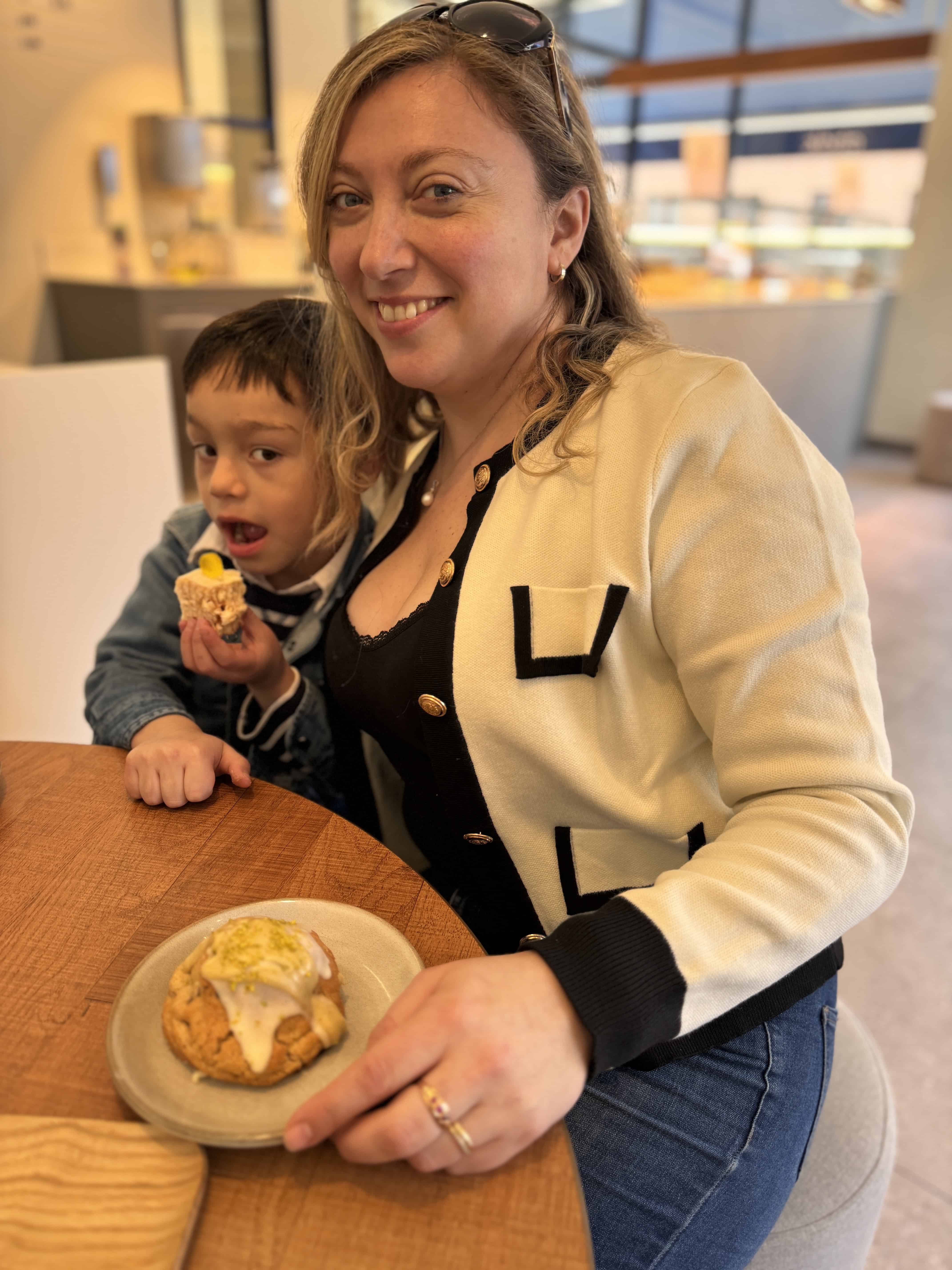 A smiling woman and child sit at a table with pastries, enjoying a treat in a bright café reminiscent of MSC Fantasia dining.