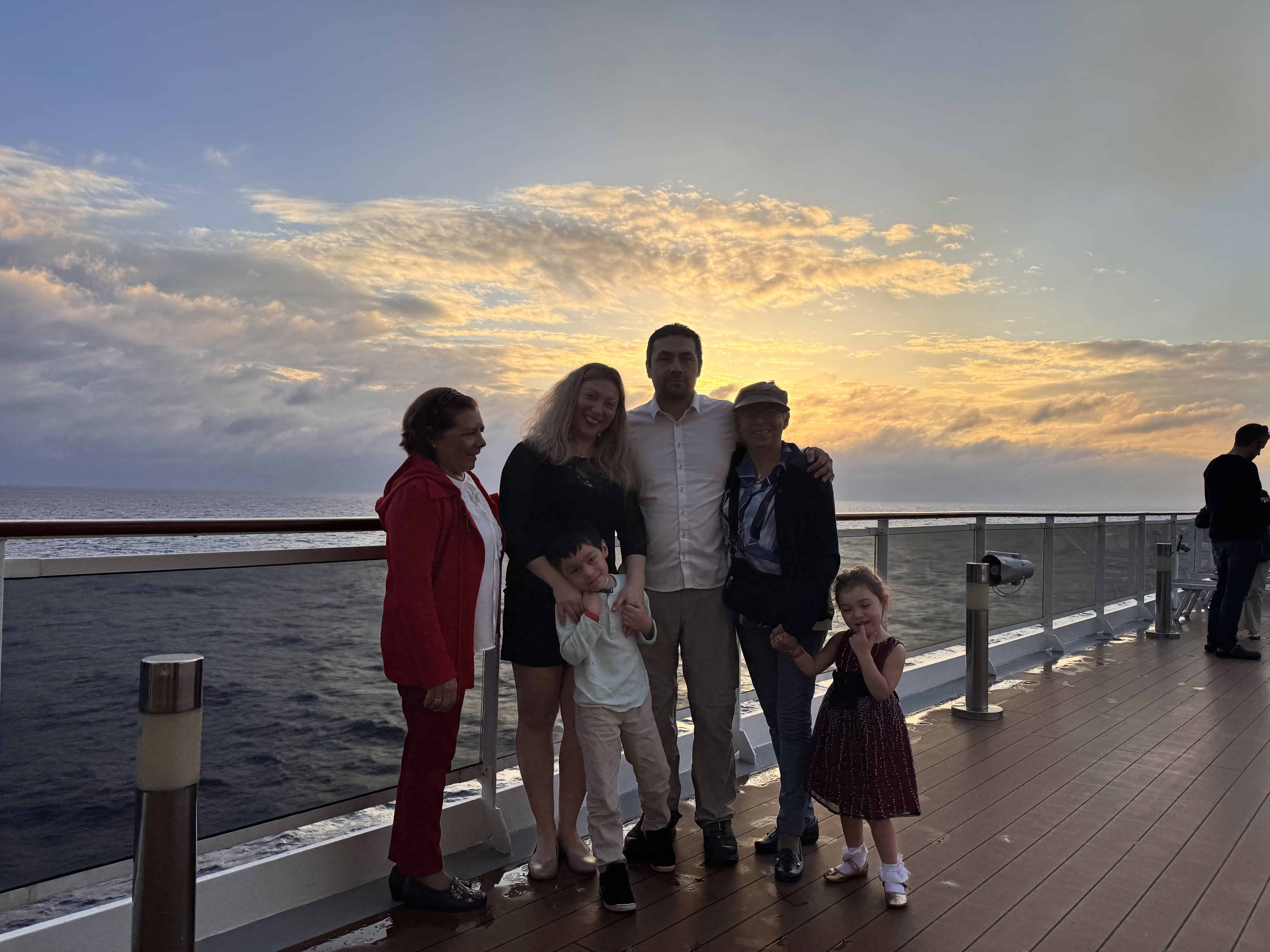 Six people pose on the deck of MSC Cruise Fantasia at sunset, with the ocean and clouds in the background.