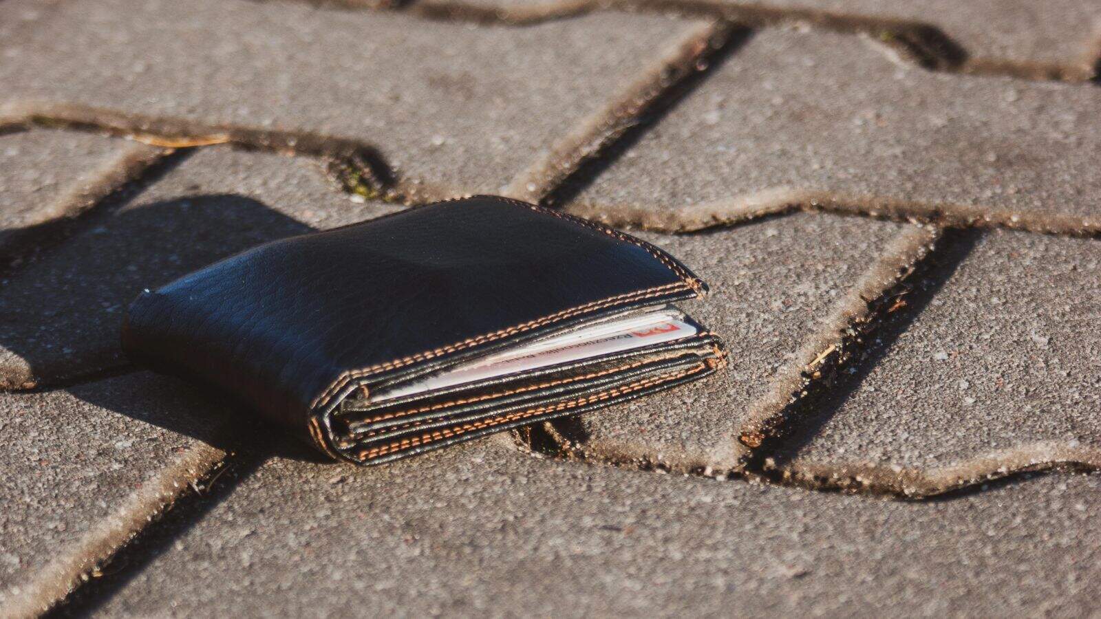A black leather wallet with visible cards inside, one of the commonly lost items at U.S. airports, lies on a sunlit, gray stone pavement.