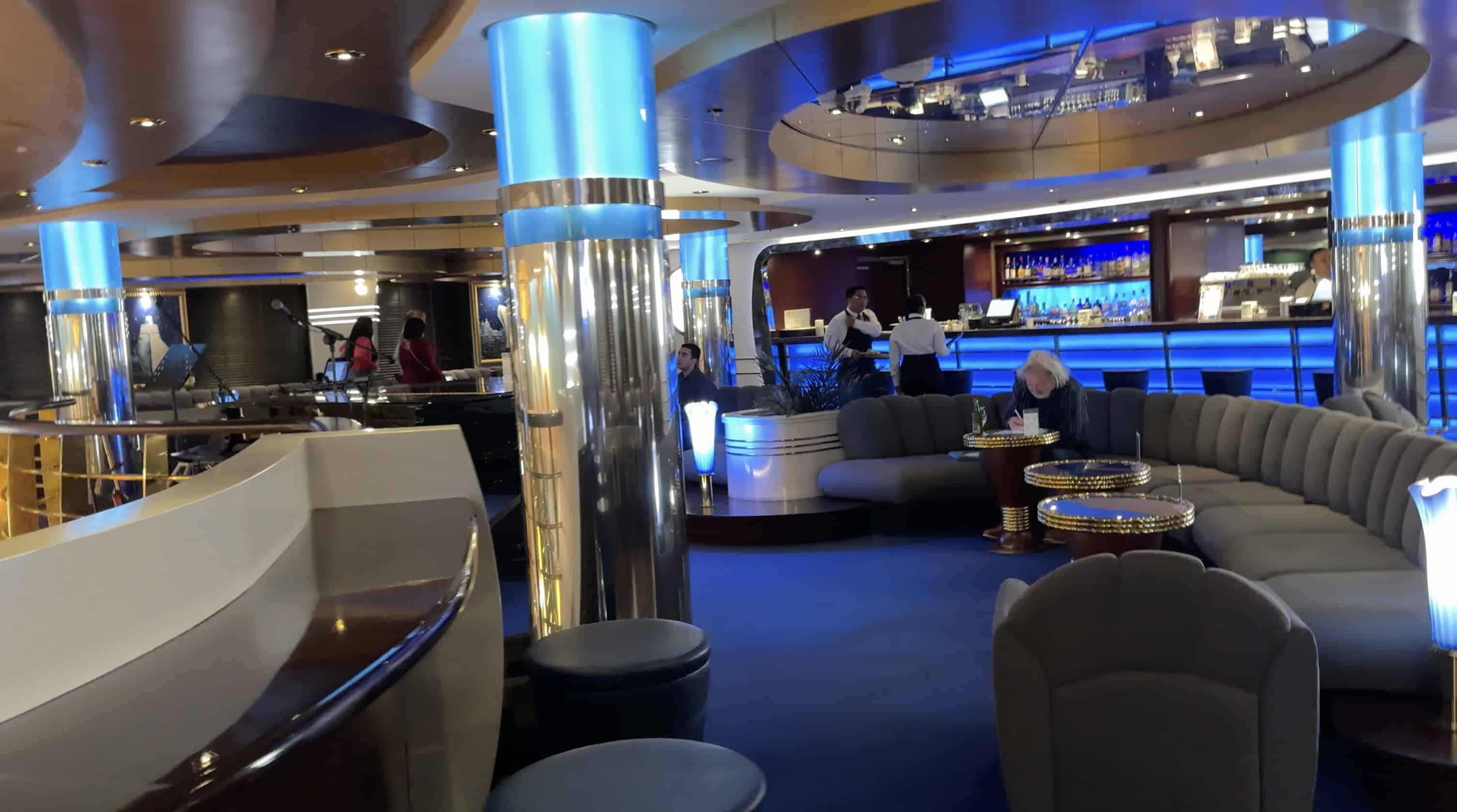 A modern lounge on the MSC Fantasia cruise with blue lighting, round seats, and people sitting and chatting near a bar area—perfect for your 2025 cruise review.