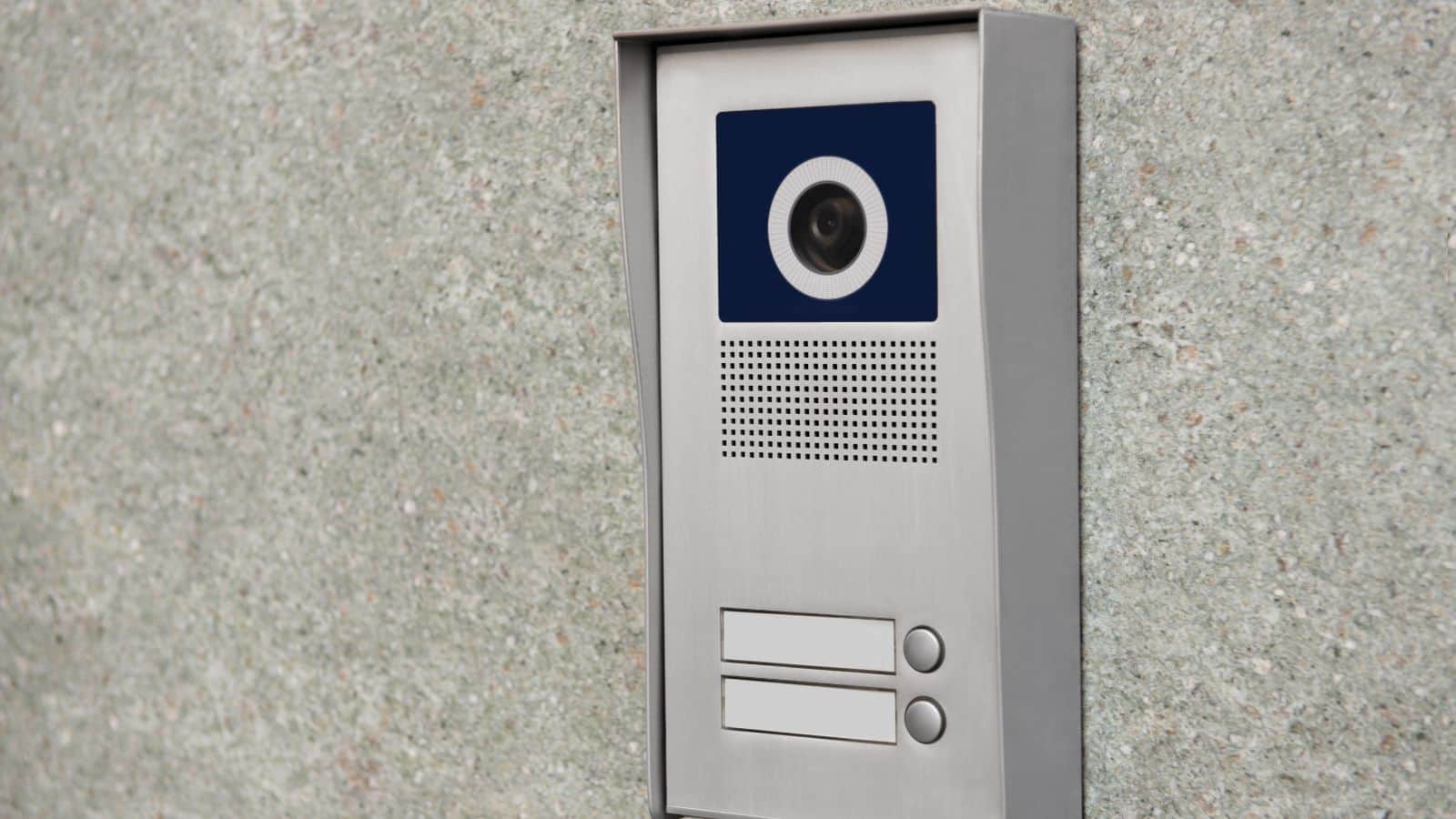 A silver intercom system with a camera and buttons mounted on a textured gray wall.