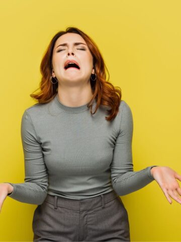 Woman in a gray top shrugging and making a frustrated face against a yellow background, capturing the mood of cruise complaints about disappointing cruise food.