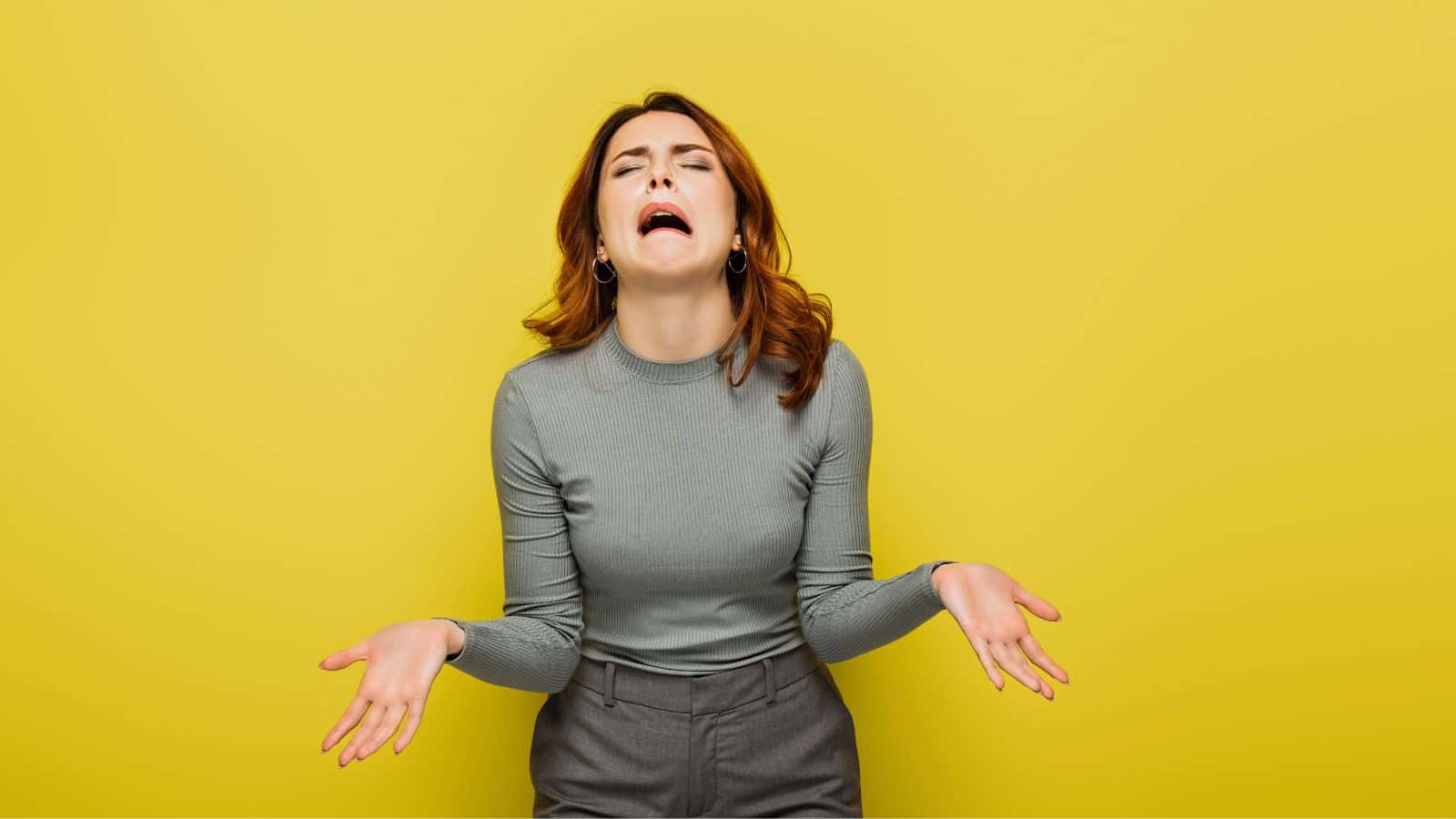 Woman in a gray top shrugging and making a frustrated face against a yellow background, capturing the mood of cruise complaints about disappointing cruise food.
