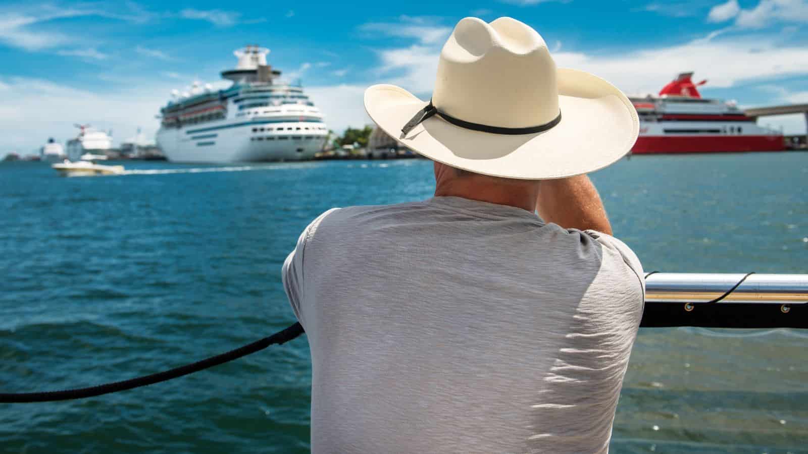 Person in a white cowboy hat looks at cruise ships on the water under a blue sky.