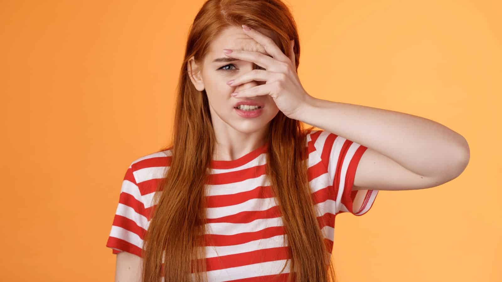 Young woman with long red hair in a striped shirt covers part of her face with her hand, looking concerned—perhaps after realizing she made one of the common tourist mistakes in Paris.