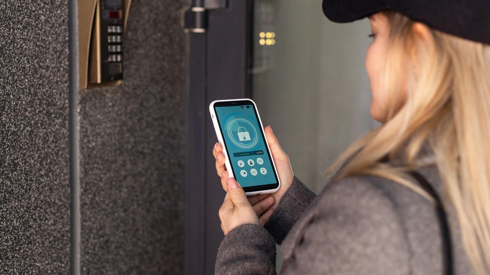 Woman using a smartphone app to unlock a secure door with a keypad access panel next to her.