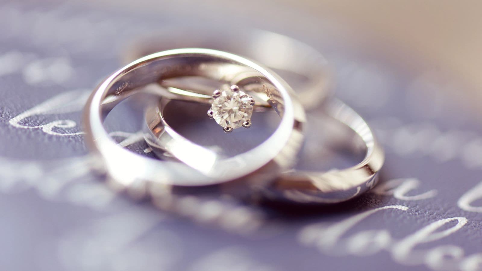 Close-up of three rings on a blurred surface with text; one ring features a diamond solitaire, while the other two are plain metal bands—jewelry like this is among the commonly lost items found at U.S. airports.