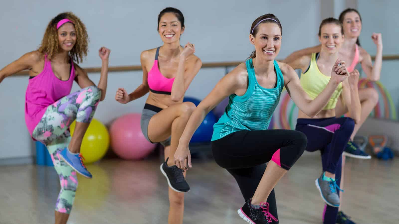 Five women in athletic wear participate in a group fitness class, raising their knees as part of an exercise routine&mdash;a perfect activity for travelers seeking wellness during all-inclusive vacations, with exercise balls and equipment in the background.