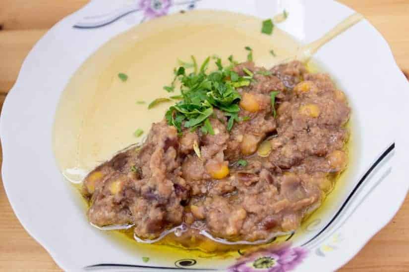 A white plate with mashed fava beans, olive oil, and fresh herbs garnished on top.